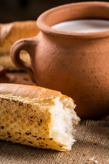 Pot en argile avec du lait et de la baguette sur une table en bois