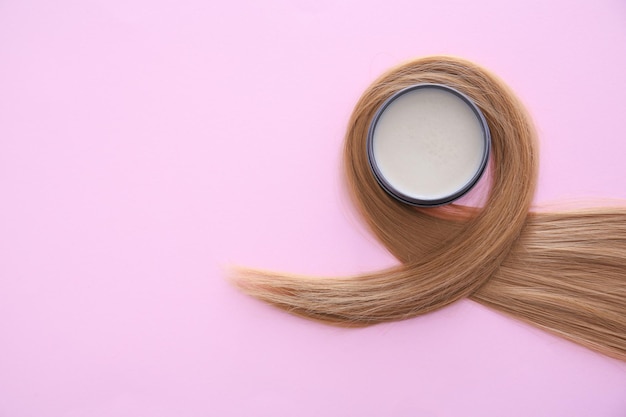 Photo pot avec de l'argile pour le coiffage et mèche de cheveux blonds sur fond de couleur