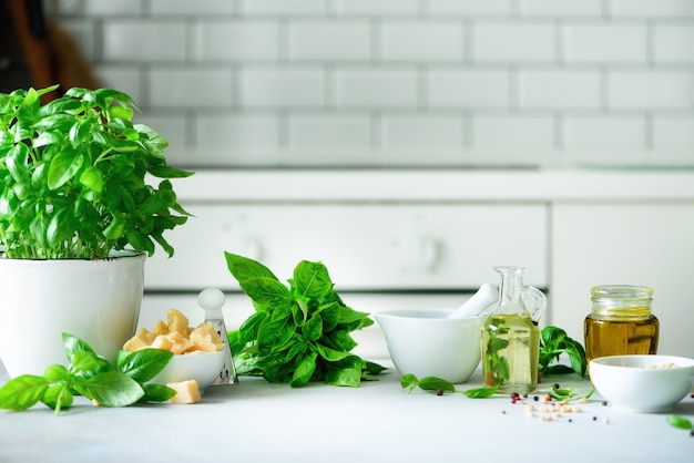 Pot de basilic frais, huile, pignons de pin, avec un fond de cuisine blanc.