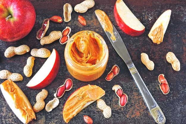 Pot de beurre d'arachide, cacahuètes en pelure, tranches de pomme et couteau. Pommes au beurre d'arachide sur une table authentique et élégante.