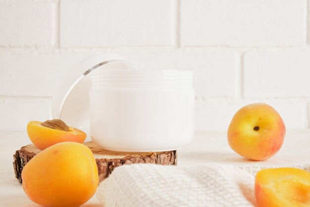 Pot blanc en plastique d'abricots pour la crème ou les cosmétiques sur un podium en bois à partir d'un bois coupé à la scie sur fond clair