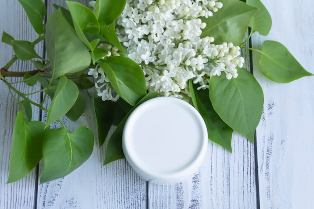 Un pot blanc avec des produits cosmétiques et des crèmes avec des fleurs de lilas fraîches et parfumées