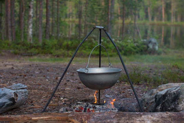 Un pot de camping est suspendu au-dessus du feu sur un trépied Cuisiner lors d'une randonnée en camping