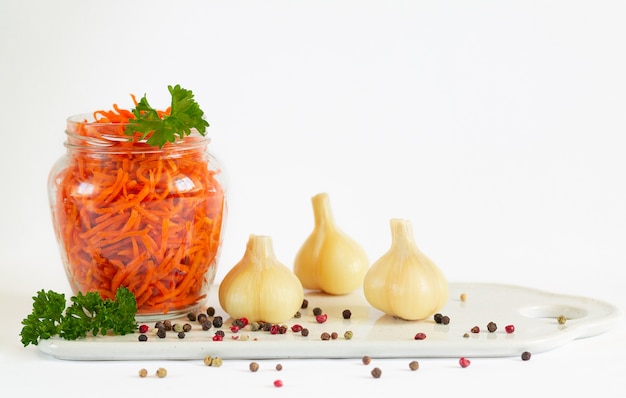 Pot de carottes fermentées à côté d'ail mariné isolé sur fond blanc avec copie espace