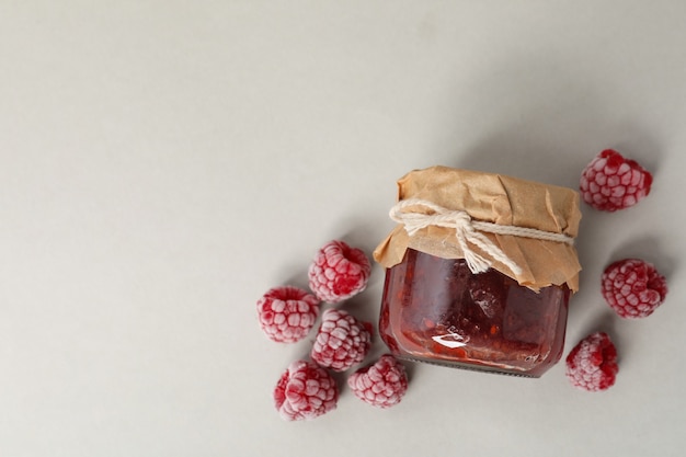 Pot de confiture de framboises avec des ingrédients sur fond gris clair