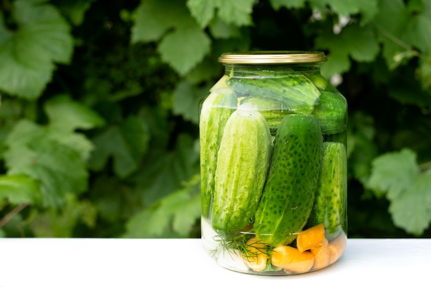 Un pot en conserve avec des concombres et des carottes est sur la table dans le jardin