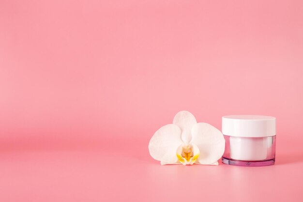 Pot cosmétique en verre avec crème avec fleur d'orchidée isolé sur fond rose