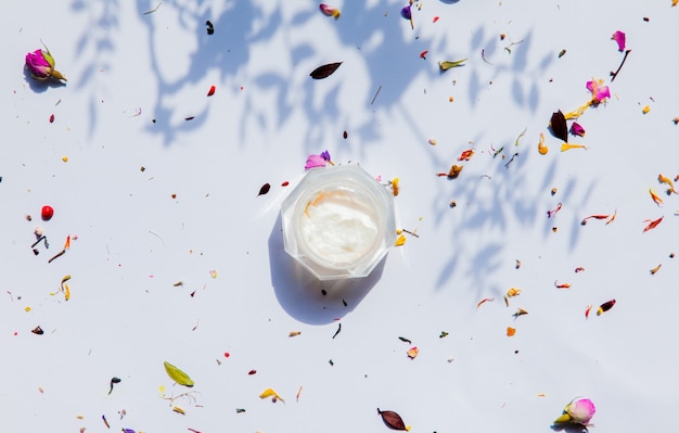 Pot de crème et fleurs sèches sur une surface blanche. Vue ci-dessus