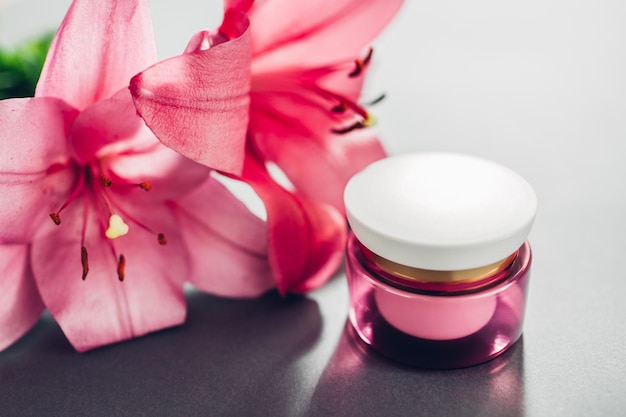 Pot de crème hydratante entouré de fleurs de lys roses sur fond gris Cosmétiques bio Soins de la peau