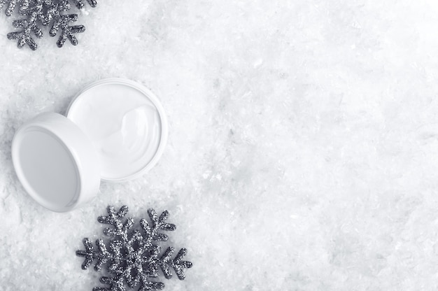 Pot de crème ouvert sur fond de vue de dessus de neige blanche.