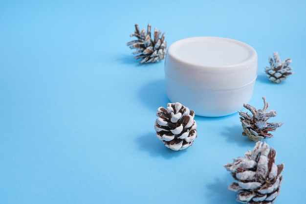 Pot de crème pour les mains yeux visage et pommes de sapin sur fond bleu Ensemble de cosmétiques pour la peau