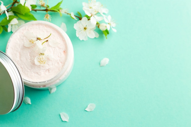 Pot de crème de soin blanc avec des fleurs de cerisier printanier fraîches