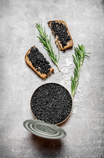 Pot avec du caviar noir et des sandwichs sur la table en pierre