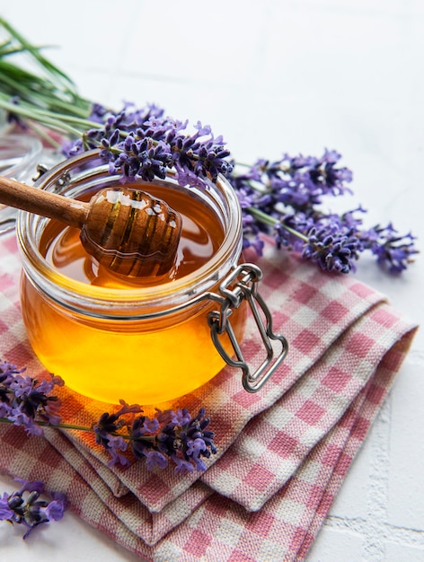 Pot avec du miel et des fleurs de lavande fraîches sur fond de carreaux blancs