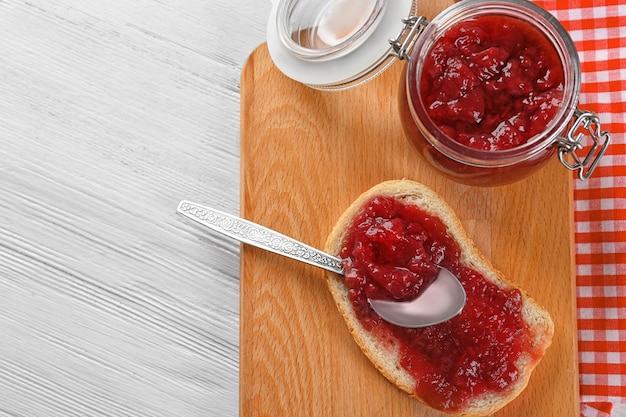 Un pot et du pain avec de la confiture de fraise sur une planche de bois