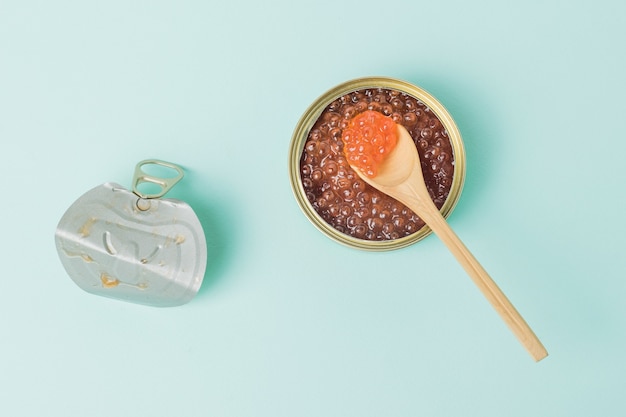 Un pot en fer avec le couvercle retiré rempli de caviar rouge sur une surface bleue. Produit marin naturel et sain.