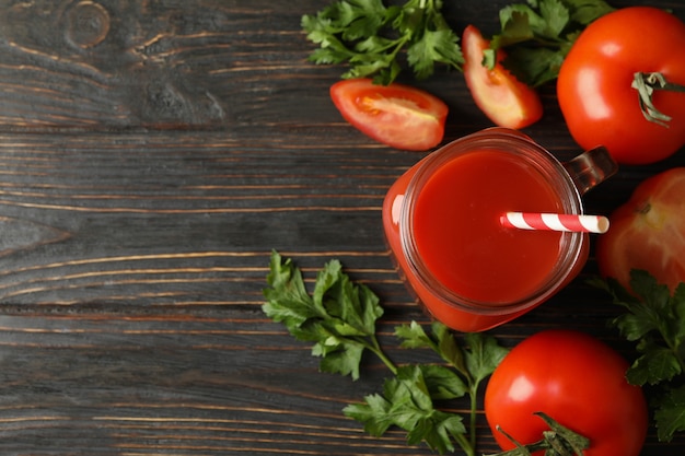 Pot de jus de tomate, tomates et persil sur bois