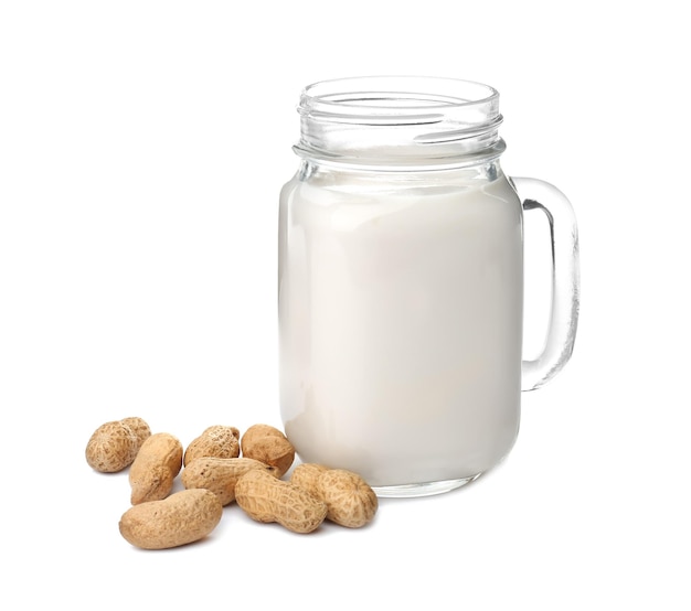 Pot Mason avec du lait d'arachide et des noix sur fond blanc