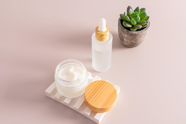 Un pot mat ouvert avec une crème hydratante sur un podium en relief en plâtre et un sérum dans une bouteille blanche mate sur un fond beige soins cosmétiques