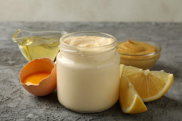 Pot avec de la mayonnaise et des ingrédients pour la cuisson sur fond gris