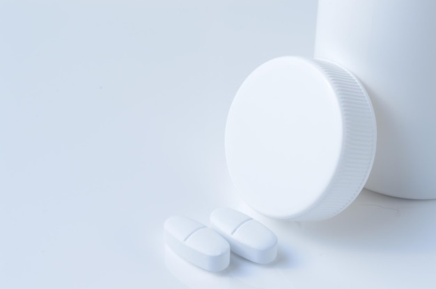 Pot de médecine en plastique blanc et fond clair de deux pilules blanches
