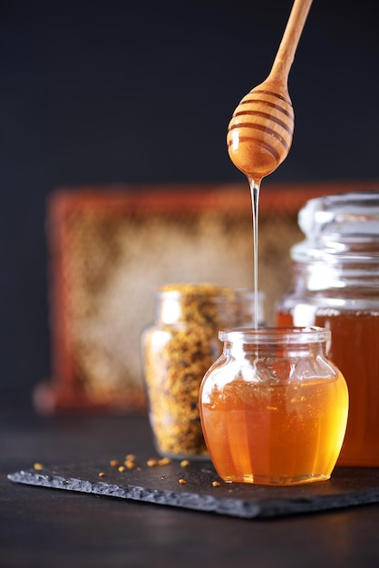 Pot de miel de granules de pollen d'abeille avec nid d'abeille compte-gouttes en bois sur fond sombre Espace de copie Concept de récolte d'automne