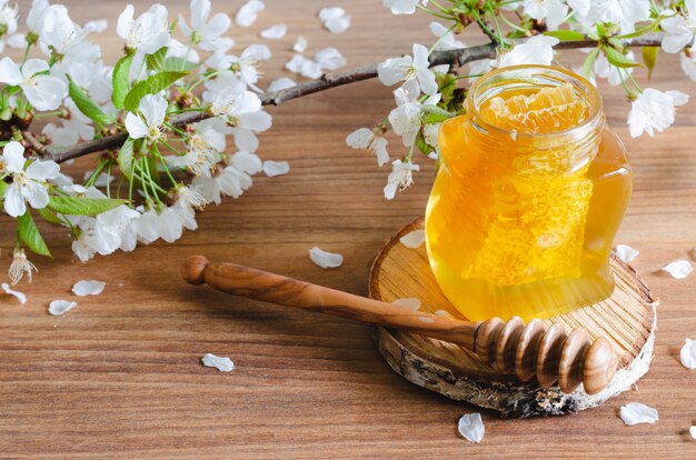 Pot de miel avec nid d'abeille et louche de miel avec des fleurs de cerisier.