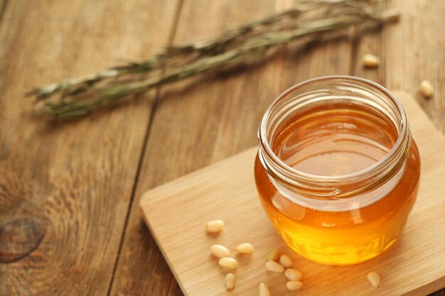 Photo un pot de miel transparent se dresse sur une planche sur une table en bois à proximité se trouvent des pignons de pin et une mise au point sélective au romarin