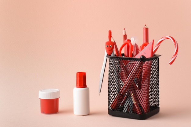 Pot noir en métal avec stylos rouges peintures et crayons sur fond rose fournitures scolaires espace pour copier