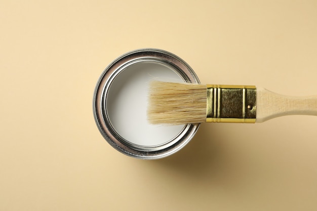 Pot de peinture et pinceau sur surface beige