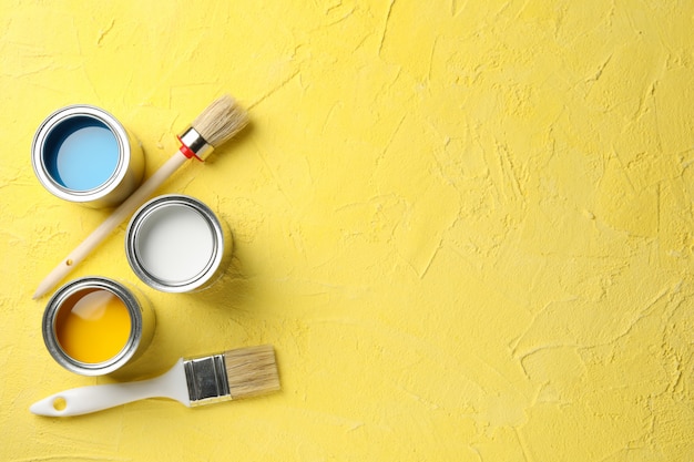 Pot de peinture et pinceaux sur fond jaune, vue de dessus