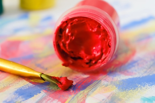 Un pot de peinture rouge aquarelle en gros plan se trouve dans le dessin à côté du pinceau Mise au point sélective