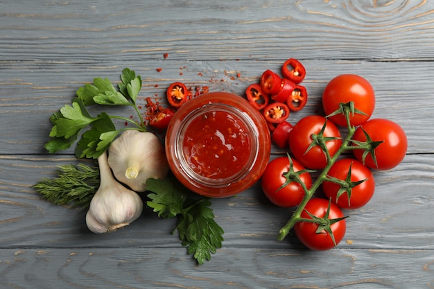 Pot avec piment rouge et sauce tomate, et épices sur table en bois