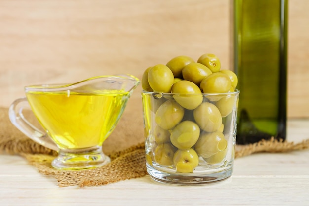 Un pot de sauce en verre avec de l'huile d'olive vierge extra et un pot d'olives vertes marinées sur un tissu de burlap sur une table en bois