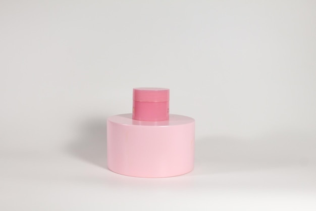 Un pot de soins de la peau avec podium rose et fond blanc