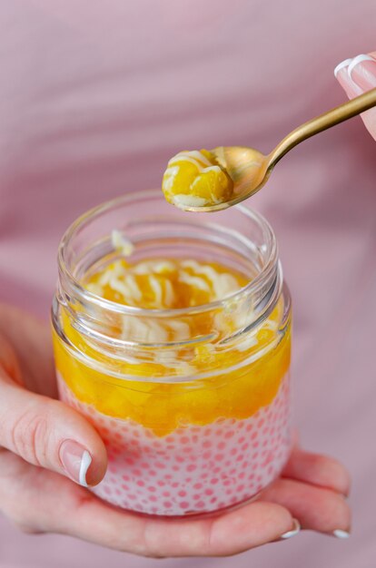 Pot de tapioca et confiture d'ananas. Une femme mange un dessert sain dans un pot avec une cuillère à café. Agréable collation appétissante - mus tendre