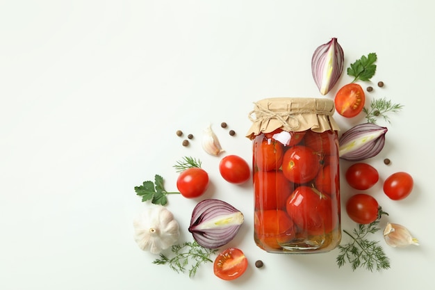 Pot de tomates marinées et ingrédients sur blanc