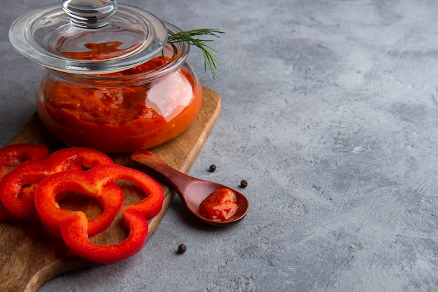 Pot en verre avec ajvar, lutenitza sur un espace gris