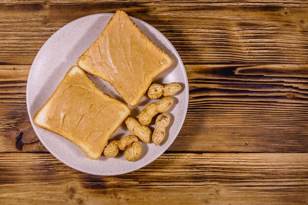 Pot en verre avec beurre de cacahuète et assiette avec sandwichs sur une table en bois Vue de dessus