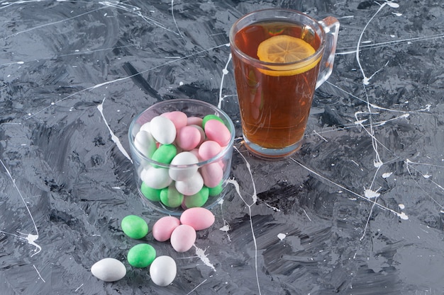 Pot en verre de bonbons colorés et tasse de thé noir sur table en marbre.