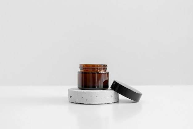 Pot en verre brun unique avec capuchon noir sur fond gris socle en béton. Crème, sérum, huile, lotion. Contenant en verre écologique zéro déchet. Produit de spa. Cosmétique bio et naturelle. Beauté, soins de la peau