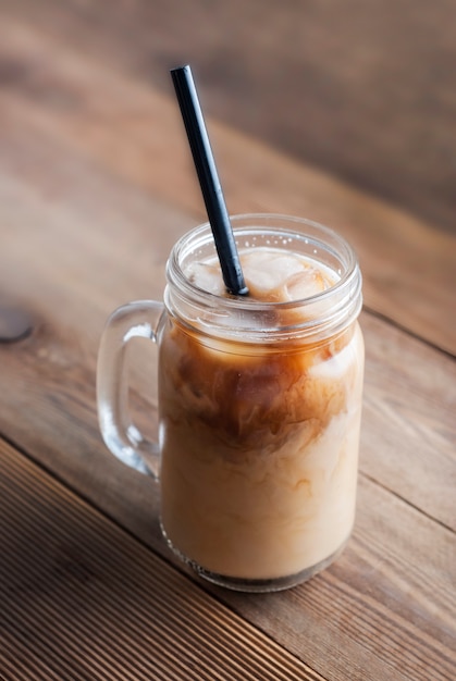 Pot en verre avec café ou boisson au lait avec glaçons et paille.