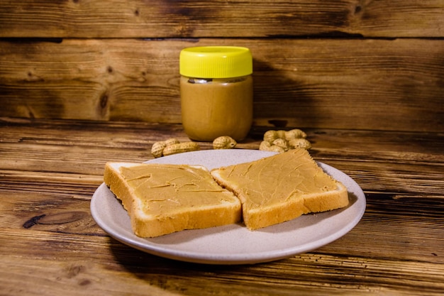 Pot en verre avec du beurre d'arachide et assiette avec des sandwichs sur une table en bois