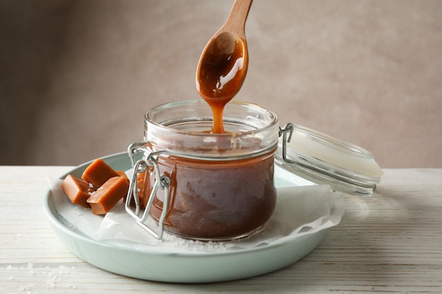 Photo pot en verre avec du caramel salé et des bonbons sur un espace en bois, espace pour le texte