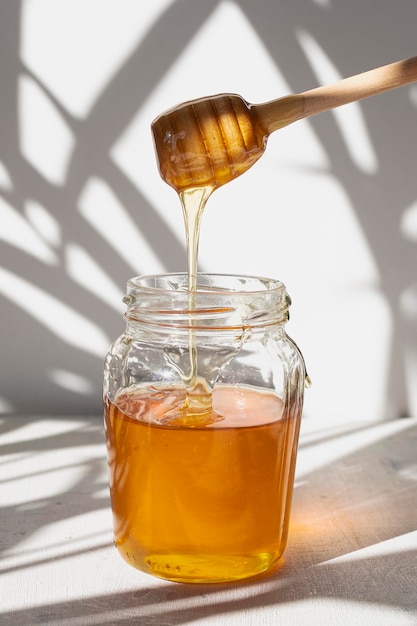 Pot en verre avec du miel cru d'abeilles avec des gouttes de miel et une cuillère à miel