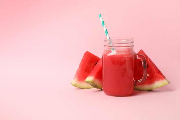 Pot en verre de jus de pastèque et tranches sur espace rose