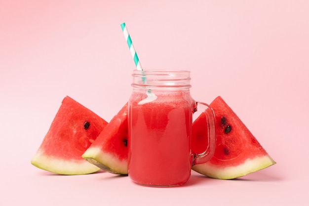 Pot en verre de jus de pastèque et tranches sur rose