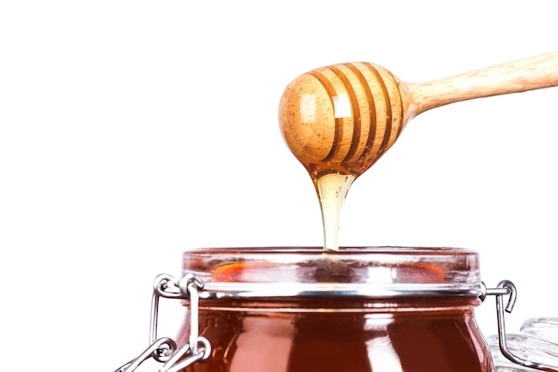 Pot en verre de miel avec coulis en bois sur fond blanc