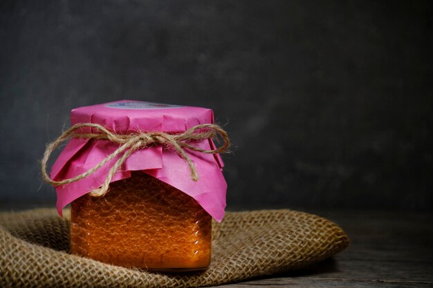 Pot en verre de miel de fraise se dresse sur de la toile de jute sur fond sombre