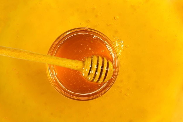 Un pot en verre de miel et une louche de miel en bois sur un fond de miel